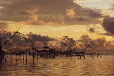 Silhouette fishing net on sea against sky during sunset