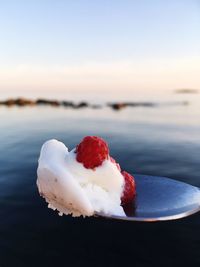 Close-up of dessert in spoon against sea and sky during sunset