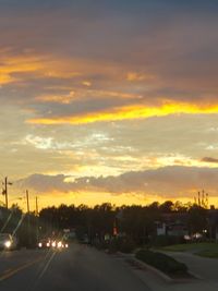 Cars on street against sky at sunset