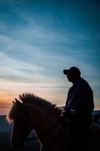 Man sitting by statue against sky during sunset