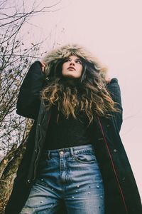 Low angle view of young woman wearing fur coat while standing against sky