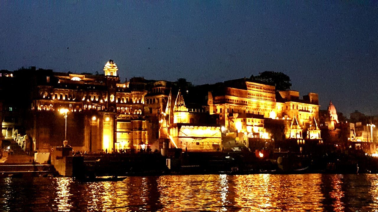 ILLUMINATED BUILDINGS BY RIVER AGAINST SKY