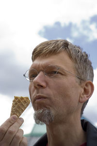 Close-up of man eating ice cream against sky