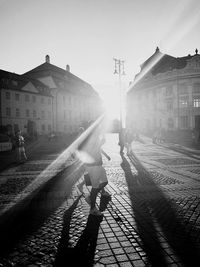 People walking on railroad track in city against clear sky