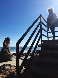 Woman standing by railing on steps at beach during sunny day