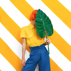 Unrecognizable model holding palm leaf and wearing vintage look on trendy striped yellow background