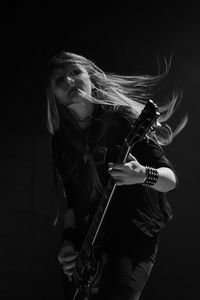 Portrait of young woman playing guitar against black background