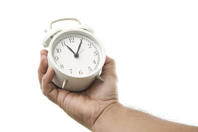 Close-up of hand holding clock against white background