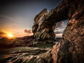 Rock formation on beach against sky during sunset