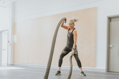 Full length portrait of smiling mature woman exercising with ropes at gym