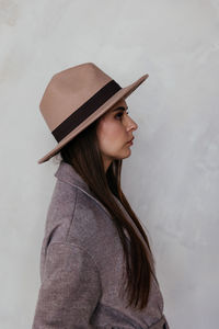 Woman in beige cashmere coat and beige hat against the background of a white wall turned sideways