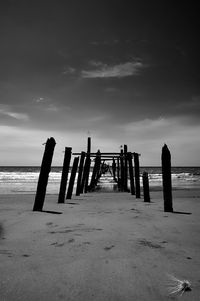 Wooden posts on pier at beach against sky