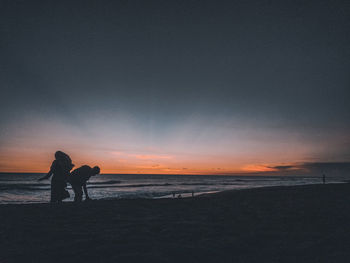 Silhouette people on beach against sky during sunset