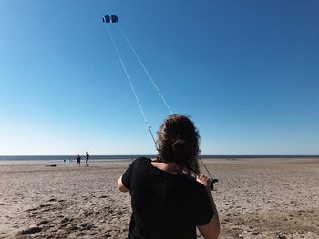 Rear view of woman flying kite on beach against clear blue sky