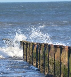 Sea waves splashing on shore against sky