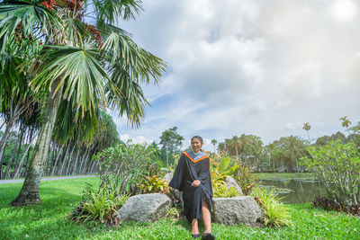 Portrait of woman wearing graduation gown sitting on rocks in park