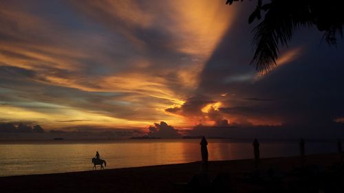 Silhouette man standing on beach against orange sky