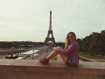 Portrait of smiling woman sitting against eiffel tower and sky