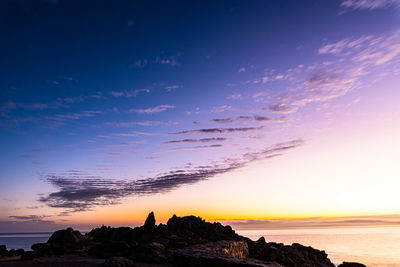 Coastal rock formations cliff silhouetted against sunrise sky and ocean bay water