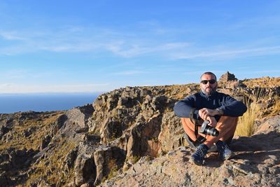 Portrait of young man on rock against sky