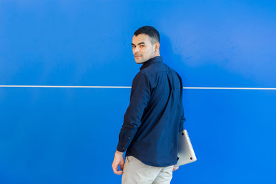 Portrait of young man standing against blue background