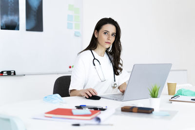 Confident female doctor working on desk in clinic