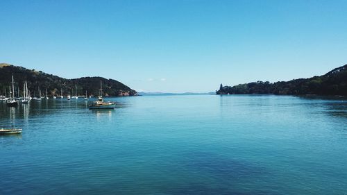 Boats in calm sea against clear blue sky