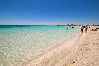 People on beach against clear blue sky