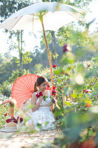 Young asian woman wearing a white dress poses with a rose in rose garden, chiang mai thailand