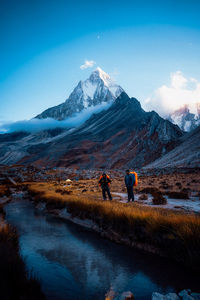 People on snowcapped mountains by lake against sky