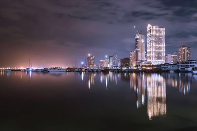 Illuminated city by sea against sky at night