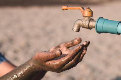 Cropped image of person cupping dirty hands below faucet