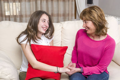 Happy mother and daughter holding hands while sitting on sofa at home