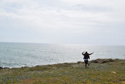 Rear view of happy woman raising her hands standing in sea against sky