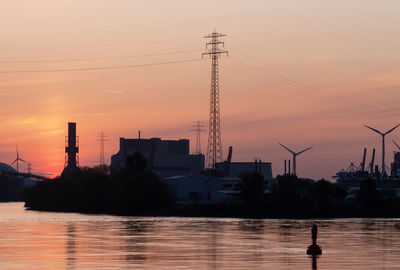 Silhouette buildings by river against sky during sunset