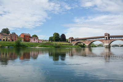 Arch bridge over river by buildings against sky