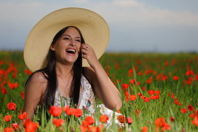 Portrait of young woman with red poppy flowers in field