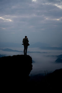 Silhouette man standing on rock against sky during sunset