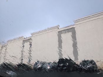 Low angle view of building seen through wet glass window