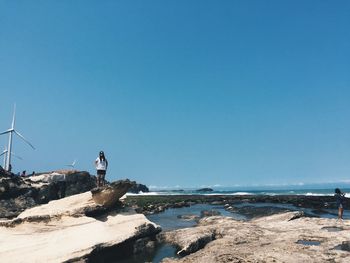 Woman sitting on rocks by sea against blue sky