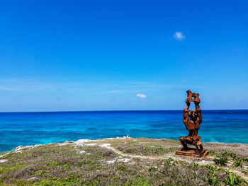 Statue on cliff by scenic sea against blue sky