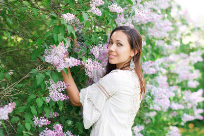 Portrait of smiling woman standing by white flowering plants