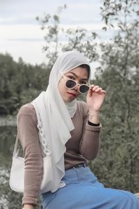 Young woman wearing sunglasses while sitting on land