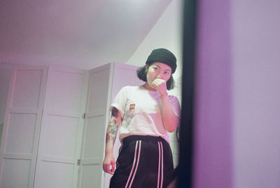 Young woman looking at camera while standing against wall at home