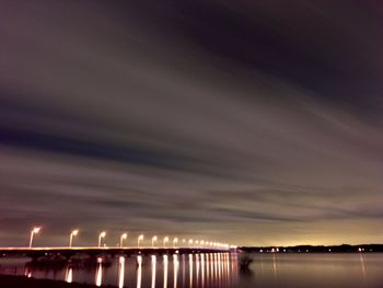 Illuminated lights by sea against sky at night