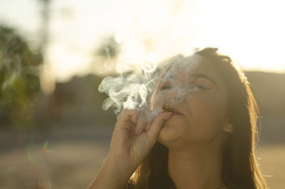 Close-up portrait of young woman smoking outdoors