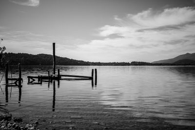 Wooden posts in lake against sky