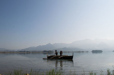 Men and boat in sea against clear sky