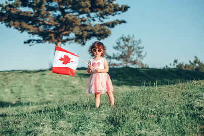 Girl holding canadian flag while standing on grass against sky