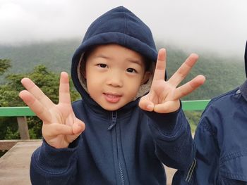 Portrait of cute boy wearing warm clothing while gesturing against mountain